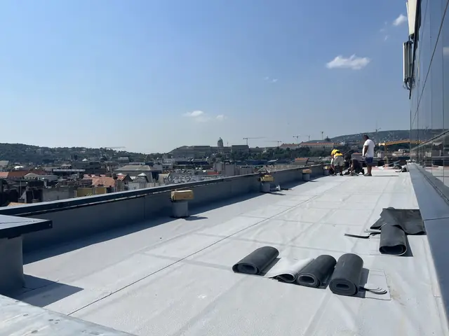 PVC lemeztekercsek a hosszú lapostetőn, az irodaház üvegfala mellett