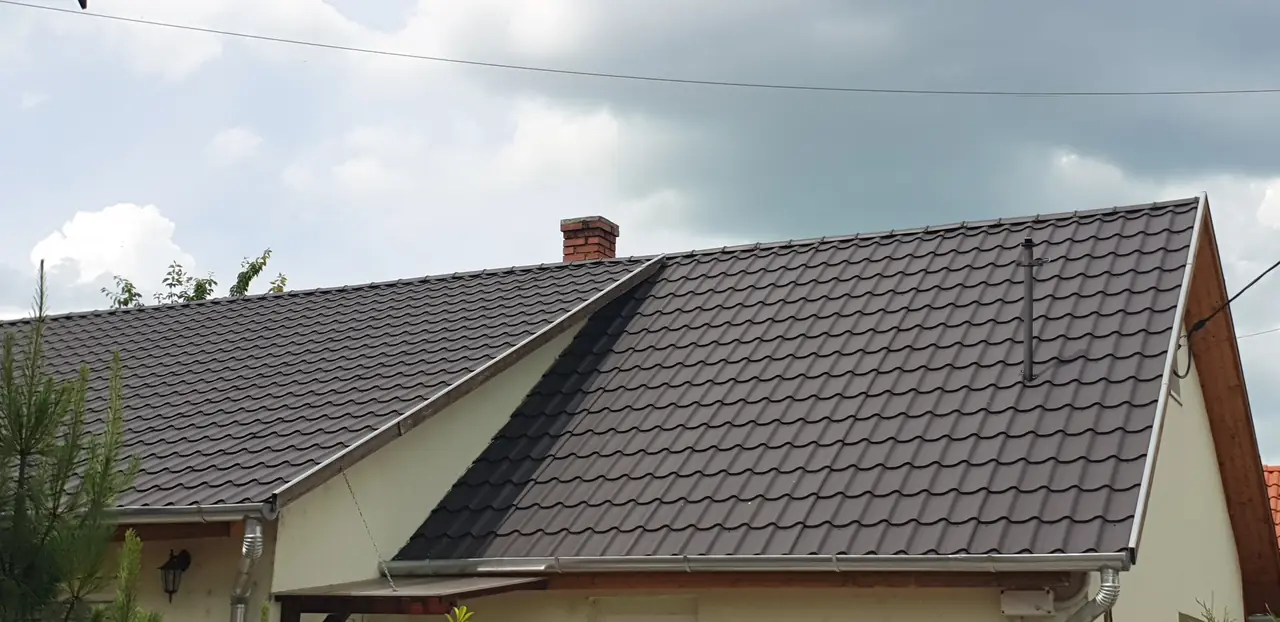 Két egymásba futó tetősík sötétbarna cserepeslemez fedéssel, vápával, oromszegéllyel, ereszcsatornával és téglakéménnyel