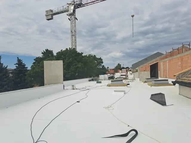 Fehér PVC lemez fektetése a lapostetőn júliusban, a háttérben a toronydaru